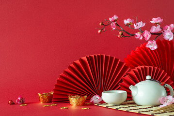 Chinese New Year side view composition: Feng shui items, teapot, tea cup, sakura blossoms, and fans artistically placed on a red background with ample space for text or advertising