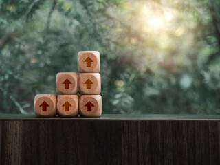 Brown rise up arrows on wooden cube blocks as a business graph or chart steps on table and green...