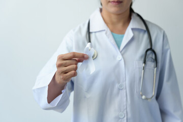 Image of a woman's hand in a doctor's uniform and stethoscope holding a white ribbon representing the struggle for life. Treated from lung cancer World cancer day concept, health insurance, prevention
