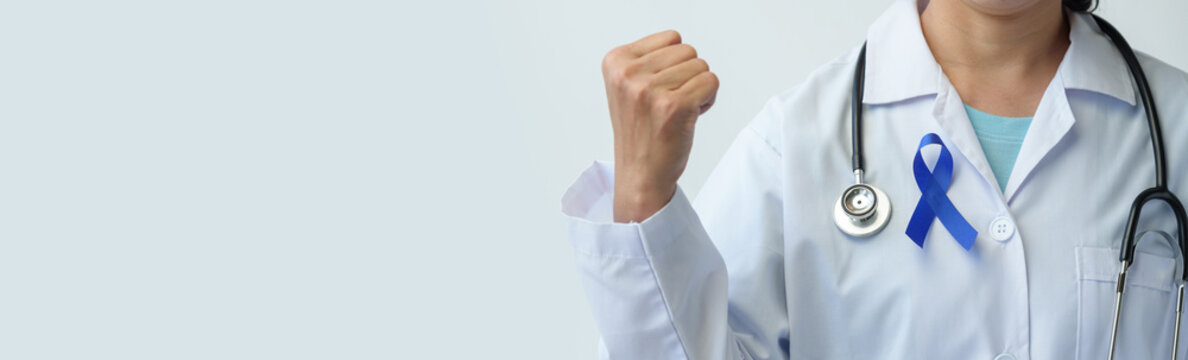 An image of a woman's hand in a doctor's uniform and stethoscope holding a blue ribbon represents fighting for life. Treatment from colon cancer World cancer day concept, copy space, banner, panorama