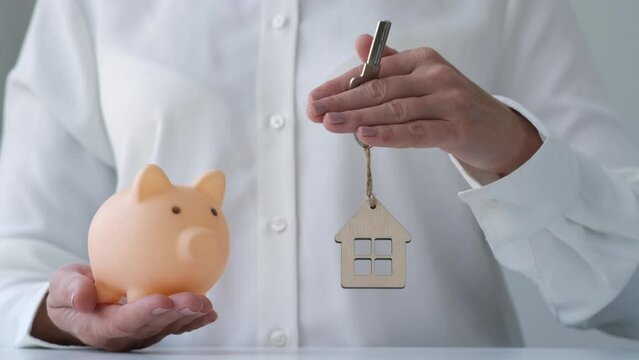 Woman hands holding piggy bank, key and keychain in shape of house representing a clock. Mortgage time concept