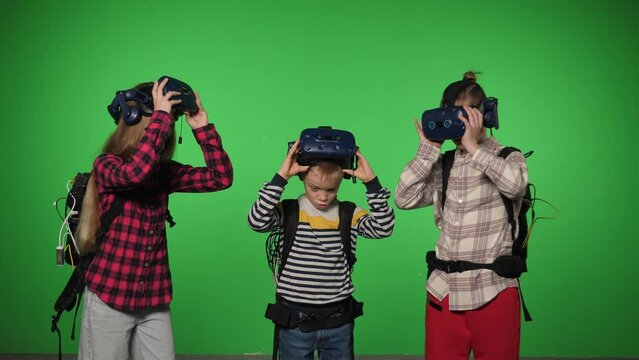 Three children take off virtual reality glasses on a green background. The children were playing virtual games. Chromakey. Teenagers lift up after playing in a virtual reality app.