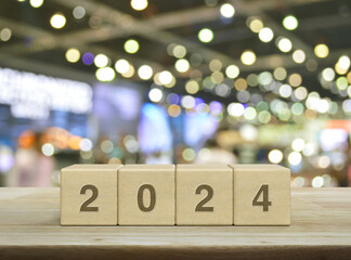 2024 letter on wood block cubes on wooden table over blur light and shadow of shopping mall, Happy...