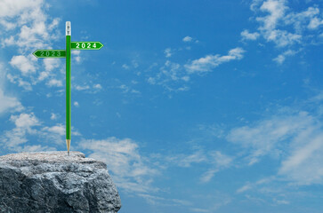 2024 and 2023 direction sign plate with green pencil on rock mountain over blue sky with white clouds, Business strategy and planning concept, Happy new year 2024 education cover