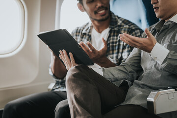 two Asian men on an airplane, looking at a tablet together, possibly friends choosing a location or...