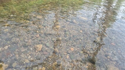 A shallow river and some river rocks. Shining colorful stone pebbles underwater. Under clear turquoise water through the stream on the pebbles. Background or texture.