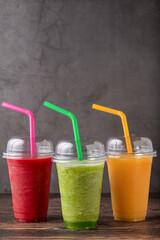 Three different fruit smoothies in plastic take away glasses on wooden background