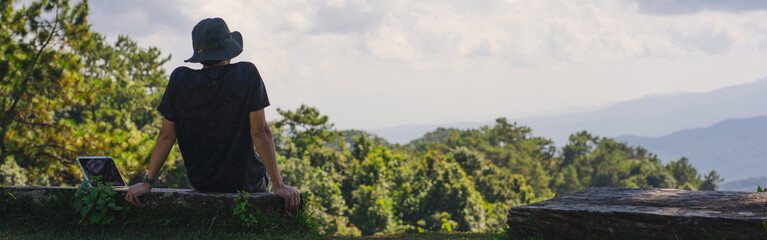 landscape and travel concept with solo freelancer man sit on wooden and use tablet work from outdoor with layer of mountain background