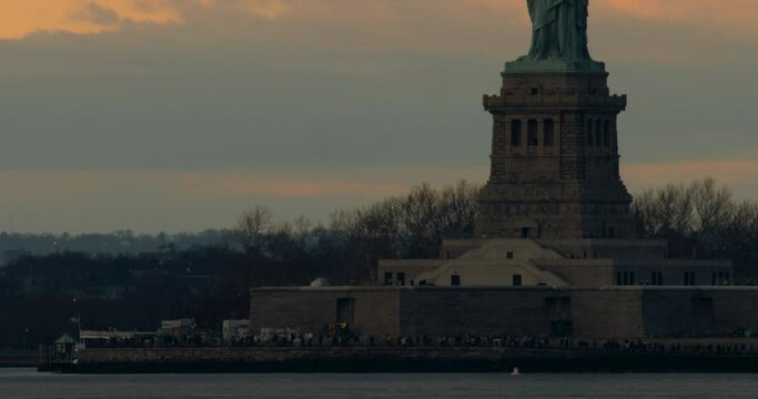 Tourists on Liberty Island Beneath Statue of Liberty Against Orange Sunset Cloud