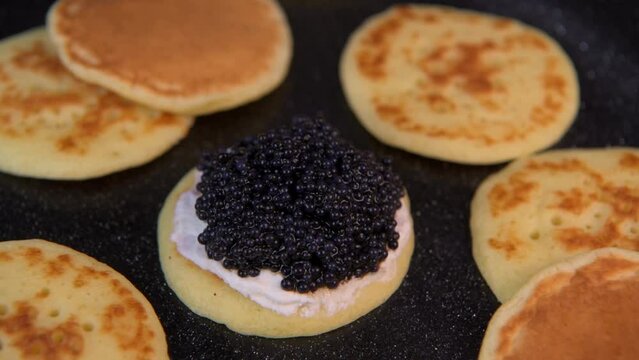 Blinis with black caviar and cream cheese, on a festive dish, mini pancakes, an elegant appetizer, High quality 4k footage