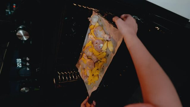 A cook is placing a tray of seasoned chicken and potatoes into the oven. The image captures the moment of cooking, suitable for a recipe tutorial or a cooking class demonstration video.
