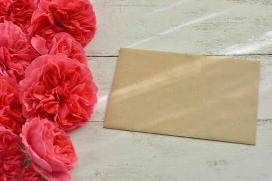 Mockup of craft paper envelope with delicate pink roses and blank  craft envelope on old white wooden background close-up. Happy Birthday, Valentine's day, wedding, Mother's Day greeting invitation ca