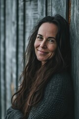 Fototapeta premium A woman with a smile on her face leaning against a wooden wall. Perfect for lifestyle or casual themes