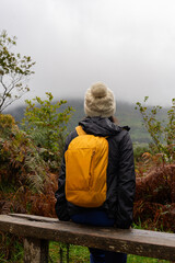 Unrecognizable young woman with knit hat and backpack enjoying a beautiful idyllic autumn landscape in the heart of Ireland with fog in the background