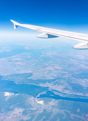Fototapeta premium Aerial view from airplane window above green ground. View from the airplane window with beautiful clouds at sunrise