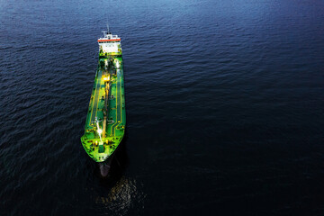 Small illuminated tanker ship with green deck in the dark blue ocean water. Aerial view. Oil and...