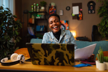 Delighted afro american dark skinned woman working online sitting in front of the laptop smiling...