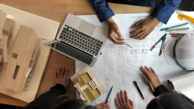 Engineer and Architect Team look at building blueprint from above. Top view of a group of businesspeople talking about blueprints when brainstorming in a meeting using a laptop and calculator.