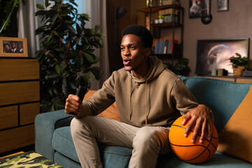 African American blogger's love for basketball, as he holds the ball in his living room and shares his passion for the game with his audience, while smiling warmly at camera.