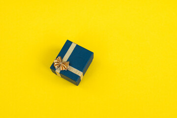 A small gift box with a gold ribbon and a bow on a yellow background. Gift