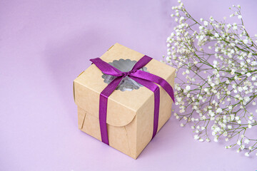 Gift craft box with ribbon on purple background with small white gypsophila flowers