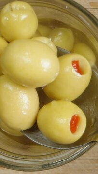 Vertical video. Using a spoon, I take a handful of salted olives with pepper from the jar and throw them back. Top view, in slow motion.