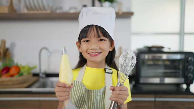 Asian child practicing to be a chef. Little asian girl in apron holding kitchen equipment on hands dancing and smiling to camera. Happy Little cute asian girl. Concept for cooking learning for kid