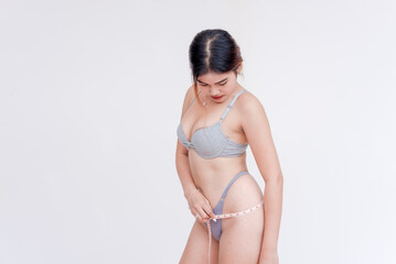 A young asian woman checks and measures her hip measurement. Wearing only gray bra and panties....