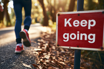Keep going concept image with red Keep going sign and legs of a runner doing jogging in a park - obrazy, fototapety, plakaty