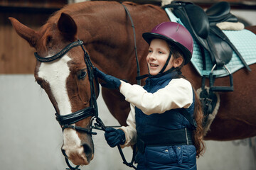 Little girl, kid in helmet taking care after horse, showing her love. Child training horseback...