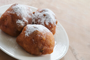 Typical dutch food commonly known as dutch doughnuts, dutchies or oliebollen with currants and powdered sugar on a white plate. Traditionally eaten on new year's eve in the Netherlands.