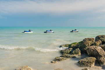 Three Jetskis, moored just off shore. The day is sunny