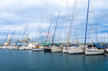 boats and yachts on pier in marine city port with masts and bulidings and blue sky on background ,...