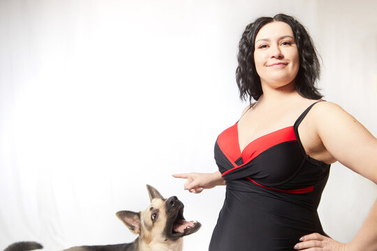 Attractive confident fat woman in a swimsuit training big dog shepherd on white background. Body positive, selfie. Funny plus size model
