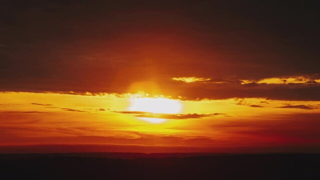 Timelapse sunset above the horizon in orange sky with dramatic clouds. 4K. Bright sun setting down above the horizon. Colorful dark sunset epic clouds. Vibrant color. Time-lapse. Sundown