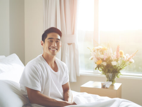 Smiling Asian man patient relaxing in bed in hospital ward