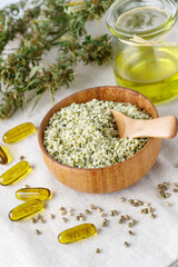 Shelled hemp seeds and oil as superfoods, supplement for eat with fiber and omega 3. Crushed cannabis seeds in wooden bowl with spoon  and cbd oil capsules on hemp fabric.