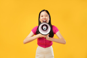 Portrait of a young Asian lady holding a megaphone and screaming, with an angry expression. Wearing...