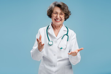 Positive attractive senior woman, doctor wearing white coat, stethoscope, looking at camera