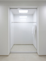 Empty white fitting room with some clothes on hanger