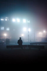 Silhouette of a man sittin down on a foggy night