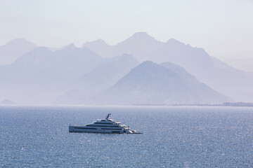 Taurus mountain silhouettes over Antalya bay in different shades of blue on a hot hazy summers day. Sole yacht on calm sea water. Antalya, Turkiye (Turkey)