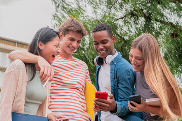 Group of students friends watching a video in the smartphone enjoying and laughing outside the campus. Young adults using the cellphone sharing social media content having fun and chatting friendly