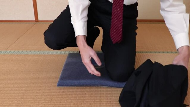 横に上着を置いて座布団の上にあぐらをかく男性