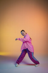 Fototapeta na wymiar A young woman in a pink shirt poses against an orange studio background. The dancer demonstrates elements of jazz-funk choreography. Modern choreography. Full length.