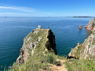 Narrow path along the edge of the cliff on the island of Shkota in August in sunny weather. Russia, Vladivostok city