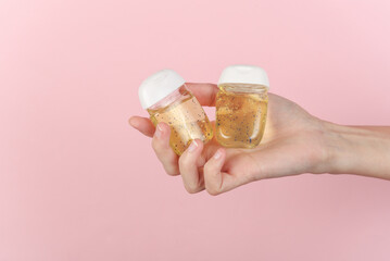 Hand holding antiseptic bottles on pink background