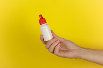 Hand holding white bottle of shoe polish on yellow background