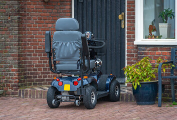 Four wheel mobility scooter parked in front of the house, a modern mobility aid vehicle in the street © Milos