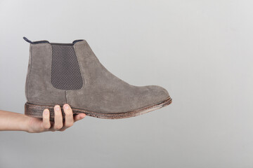 Hand holding suede Chelsea boot on gray background